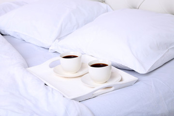 Fototapeta na wymiar Cups of coffee on comfortable soft bed with pillows
