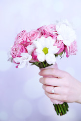 Hand holding beautiful wedding bouquet on bright background