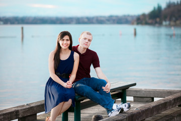 Young interracial couple sitting together on dock over lake