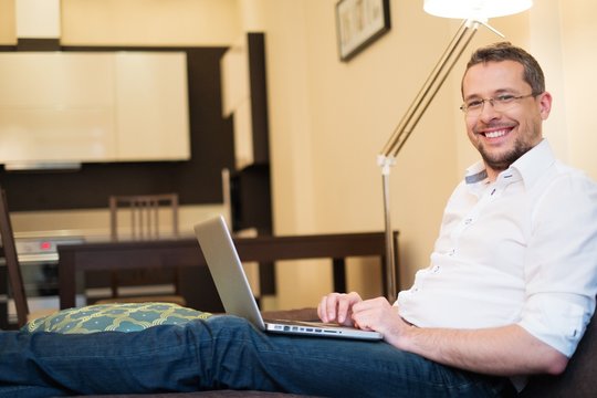 Young Man With Gray Hair With Laptop On Sofa In Home Interior