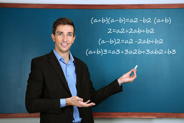 Young teacher near chalkboard in school classroom