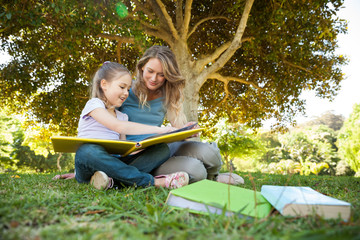 Happy mother and daughter reading a book at park