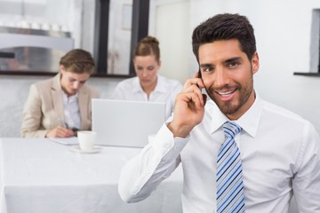 Businessman using mobile phone with colleagues at office desk