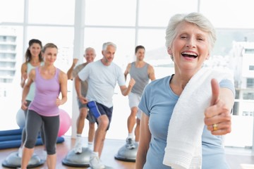 Senior woman gesturing thumbs up with people exercising