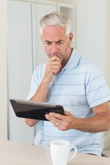 Fototapeta premium Thoughtful man using his tablet at breakfast