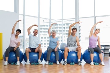 Fototapeta premium Class sitting on exercise balls and stretching hands in gym