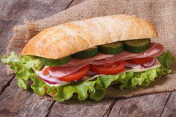 ciabatta sandwich with ham and vegetables on an old wooden table