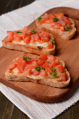 Delicious bruschetta with tomatoes on cutting board close-up