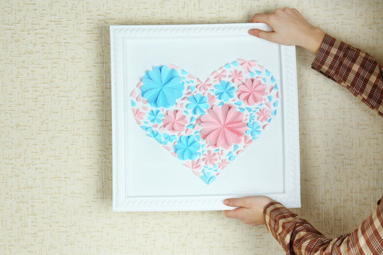 Woman hanging up picture with heart from paper flowers