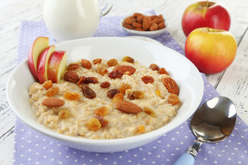 Tasty oatmeal with raisins and apples on wooden table