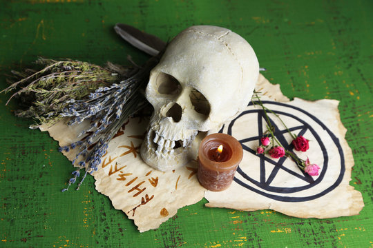 Composition with skull, old magic symbols, candle and dry herbs