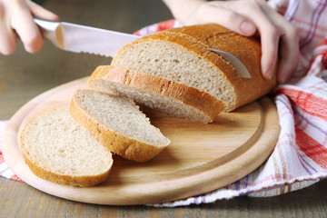 Female hands cutting bread on wooden board, close-up