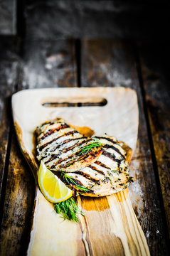 Grilled chicken with herbs and lemon on wooden background