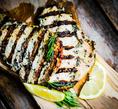 Grilled chicken with herbs and lemon on wooden background