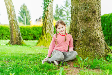 Adorable little girl sitting under the tree