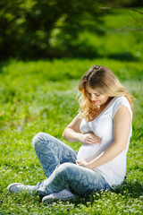 Fototapeta premium Portrait Healthy pregnant woman sitting on green grass