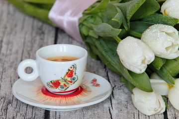Beautiful white tulips and a cup of coffee on wooden background