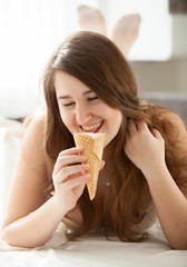 Smiling brunette woman eating ice cream at bedroom