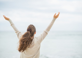 Young woman on cold beach rejoicing success. rear view