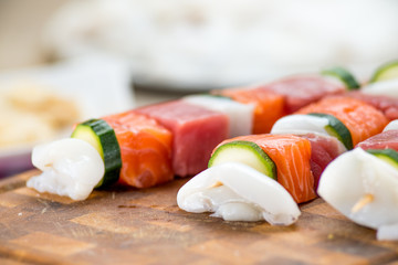 Spiedini di pesce misto crudi posti su un tagliere di legno