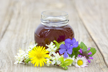 Honey in a jar and flowers on wooden background