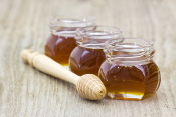 three jars of honey and honey dipper on wooden background