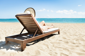 Woman Sunbathing On Deck Chair At Beach