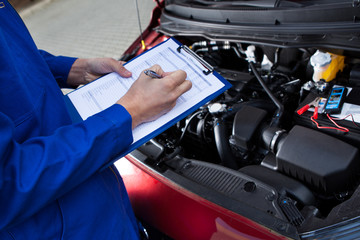 Mechanic Holding Clipboard In Front Of Open Car Engine