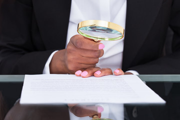 Businesswoman Using Magnifying Glass To Read Document At Desk