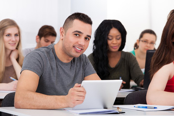 Confident Male Student Holding Digital Tablet At Desk