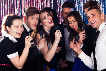 Friends Singing Into Microphones At Karaoke Party