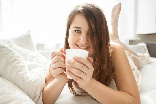 smiling woman drinking coffee in bed at morning