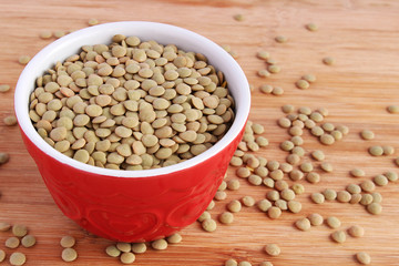 Dry green lentils in red bowl on wooden board