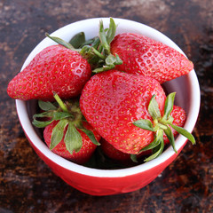 Strawberries in red bowl on brown rustic background
