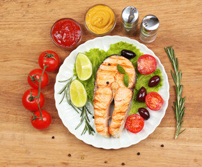 Tasty grilled salmon with vegetables, on wooden table