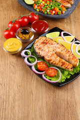 Tasty grilled salmon with lemon and vegetables, on wooden table