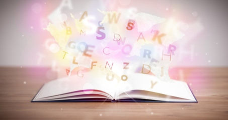 Open book with glowing letters on concrete background