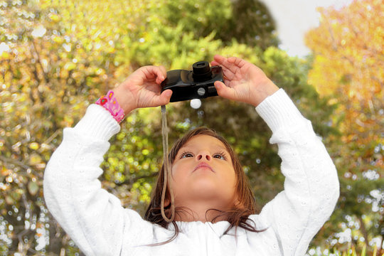 Little girl taking a picture to the digital camera outdoors