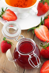 Fresh strawberry jam in glass jar with rooibos tea in white cup