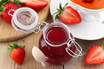 Fresh strawberry jam in glass jar with rooibos tea in white cup