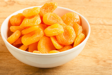 Bowl of dried apricots on wooden table background.