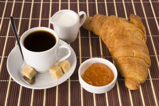 Cup of coffee, jam, croissant and cream