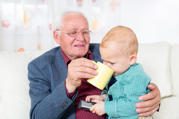 Grandfather holds small grandson on knees and gives him milk