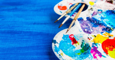 Creative background with art palette and brushes on blue canvas