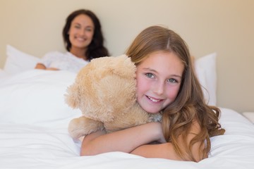 Girl embracing teddy bear with mother in background