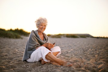 Fototapeta na wymiar Senior caucasian woman with cell phone on the beach