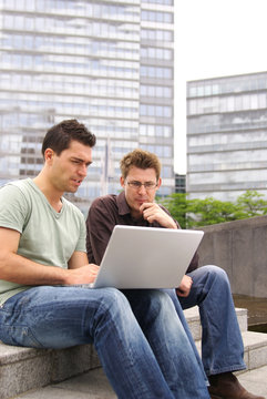 Two men working with laptop outdoors urban secene