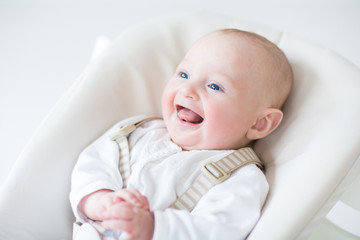 Cute laughing baby boy sitting in a high chair waiting for lunch
