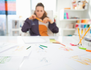 Closeup on table and thoughtful fashion designer in background