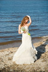 Fototapeta na wymiar Beautiful bride in a white dress on coast of river